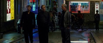 Movie still from “Premium Rush” (2012), directed by David Koepp – A group of men standing on the sidewalk at night; Medium shot, Low angle