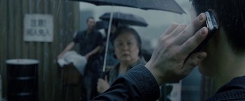 Movie still from “Premium Rush” (2012), directed by David Koepp – An older woman holding an umbrella over her head; Close Up shot, Over the shoulder angle