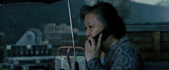 Movie still from “Premium Rush” (2012), directed by David Koepp – An older woman holding an umbrella while talking on a phone; Close Up shot, High angle