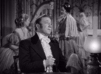 Movie still from “Pride and Prejudice” (1940), directed by Robert Z. Leonard – A man in a suit sitting in front of a group of people; Medium shot, Over the shoulder angle