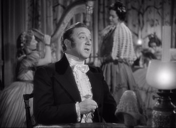 Movie still from “Pride and Prejudice” (1940), directed by Robert Z. Leonard – A man wearing a suit and a bow tie in front of a crowd; Medium shot, Over the shoulder angle