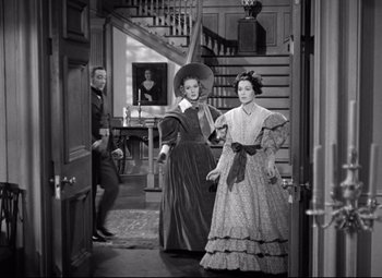 Movie still from “Pride and Prejudice” (1940), directed by Robert Z. Leonard – A man and a woman dressed in period clothing in front of a staircase; Wide shot, Over the shoulder angle