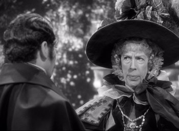 Movie still from “Pride and Prejudice” (1940), directed by Robert Z. Leonard – An older woman wearing a large hat and looking at a younger man; Close Up shot, Over the shoulder angle