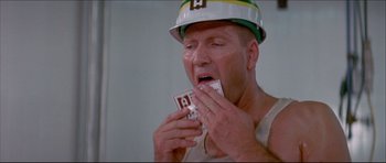 Movie still from “Prime Cut” (1972), directed by Michael Ritchie – A man in a hard hat is holding a piece of paper in his mouth; Close Up shot, Low angle