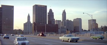 Movie still from “Prime Cut” (1972), directed by Michael Ritchie – Cars driving down a street past a city skyline; Extreme Wide shot, High angle