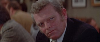Movie still from “Prime Cut” (1972), directed by Michael Ritchie – An older man in a suit and tie looking at the camera; Close Up shot, Over the shoulder angle