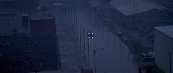 Movie still from “Prime Cut” (1972), directed by Michael Ritchie – A car driving down a street in the rain; Extreme Wide shot, High angle
