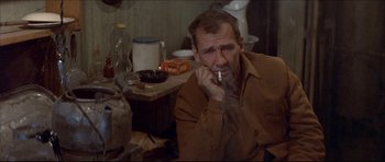 Movie still from “Prime Cut” (1972), directed by Michael Ritchie – A man smoking a cigarette while sitting in a room; Medium shot, Over the shoulder angle