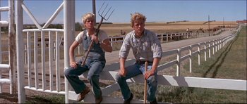 Movie still from “Prime Cut” (1972), directed by Michael Ritchie – A couple of men sitting next to each other on a fence; Medium shot, Low angle