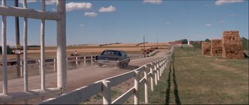 Movie still from “Prime Cut” (1972), directed by Michael Ritchie – A car driving down a dirt road next to a wooden fence; Wide shot, Over the shoulder angle