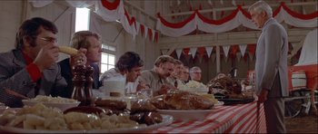 Movie still from “Prime Cut” (1972), directed by Michael Ritchie – A group of people sitting at a table with plates of food on it; Wide shot, Over the shoulder angle
