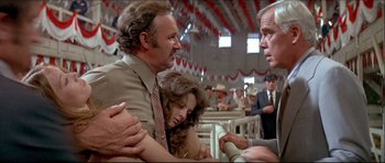 Movie still from “Prime Cut” (1972), directed by Michael Ritchie – A man and a woman are holding hands while another man is talking to another man; Medium shot, Low angle