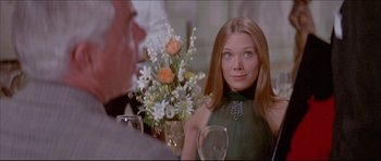 Movie still from “Prime Cut” (1972), directed by Michael Ritchie – A woman sitting at a table with a vase of flowers in front of her; Close Up shot, Over the shoulder angle