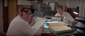 Movie still from “Prime Cut” (1972), directed by Michael Ritchie – A man sitting at a desk holding a piece of paper; Close Up shot, Over the shoulder angle
