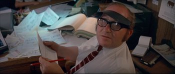 Movie still from “Prime Cut” (1972), directed by Michael Ritchie – A man wearing glasses and a hat is writing; Close Up shot, High angle