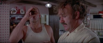 Movie still from “Prime Cut” (1972), directed by Michael Ritchie – Two men in a room one is eating a donut and the other is drinking from a cup; Close Up shot, Low angle