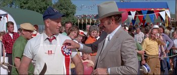 Movie still from “Prime Cut” (1972), directed by Michael Ritchie – A man in a suit and a hat is holding a ribbon; Medium shot, Over the shoulder angle