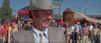 Movie still from “Prime Cut” (1972), directed by Michael Ritchie – A man in a suit and a cowboy hat is smiling; Medium shot, Over the shoulder angle