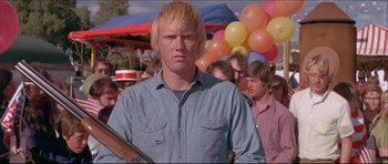 Movie still from “Prime Cut” (1972), directed by Michael Ritchie – A man with blonde hair holding a rifle in front of a crowd; Close Up shot, Low angle