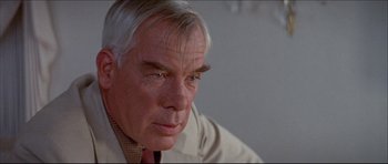 Movie still from “Prime Cut” (1972), directed by Michael Ritchie – An older man wearing a suit and tie looking down; Close Up shot, Over the shoulder angle
