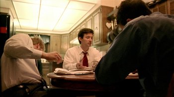 Movie still from “Primer” (2004), directed by Shane Carruth – A man sitting at a table in front of two other men; Medium shot, Over the shoulder angle