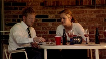Movie still from “Primer” (2004), directed by Shane Carruth – A man and a woman sitting at a table with drinks; Medium shot, Over the shoulder angle