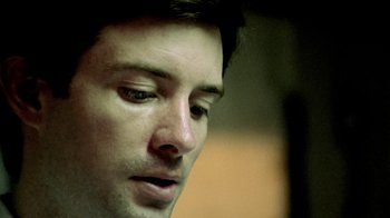 Movie still from “Primer” (2004), directed by Shane Carruth – A man's face in a dimly - lit room; Extreme Close Up shot, Low angle