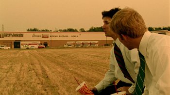 Movie still from “Primer” (2004), directed by Shane Carruth – Two men sitting in a field eating a hot dog and drinking a drink; Extreme Wide shot, Low angle