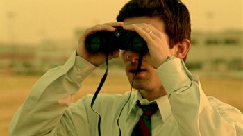 Movie still from “Primer” (2004), directed by Shane Carruth – A man looking through a pair of binoculars; Close Up shot, High angle