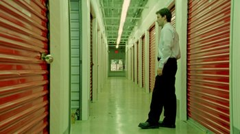 Movie still from “Primer” (2004), directed by Shane Carruth – A man standing in an aisle of a storage unit; Wide shot, Low angle