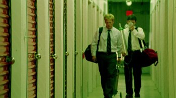 Movie still from “Primer” (2004), directed by Shane Carruth – Two young men walking down a hallway with suitcases; Wide shot, Low angle