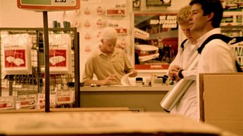 Movie still from “Primer” (2004), directed by Shane Carruth – A man is standing at a counter in a store; Wide shot, Low angle