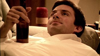 Movie still from “Primer” (2004), directed by Shane Carruth – A man laying on a bed holding a bottle of beer; Close Up shot, High angle