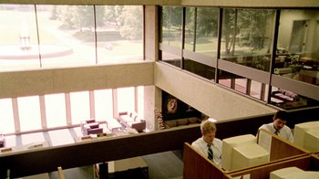 Movie still from “Primer” (2004), directed by Shane Carruth – A man sitting in front of a window in a room; Wide shot, Low angle