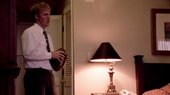 Movie still from “Primer” (2004), directed by Shane Carruth – A man standing in front of a lamp in a room; Medium shot, Low angle