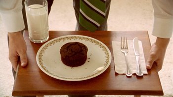 Movie still from “Primer” (2004), directed by Shane Carruth – A plate with a cupcake on top of it on a wooden table; Extreme Close Up shot, Overhead angle