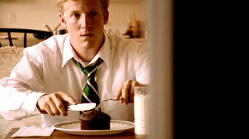 Movie still from “Primer” (2004), directed by Shane Carruth – A man in white shirt and tie cutting a chocolate cake; Close Up shot, Over the shoulder angle