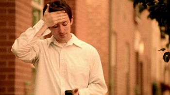 Movie still from “Primer” (2004), directed by Shane Carruth – A man holding his head while looking at his cell phone; Close Up shot, Low angle