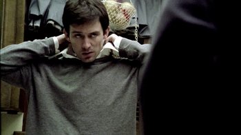 Movie still from “Primer” (2004), directed by Shane Carruth – A man in a gray shirt is holding his hands behind his head; Close Up shot, Over the shoulder angle
