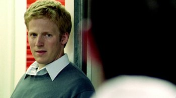 Movie still from “Primer” (2004), directed by Shane Carruth – A man with blonde hair wearing a white collared shirt; Close Up shot, Over the shoulder angle