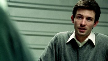 Movie still from “Primer” (2004), directed by Shane Carruth – A man wearing a gray sweater is looking at the camera; Close Up shot, Over the shoulder angle