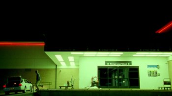 Movie still from “Primer” (2004), directed by Shane Carruth – A man sitting on the ground in front of a building; Extreme Wide shot, Low angle