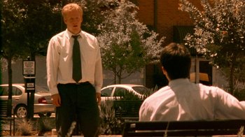 Movie still from “Primer” (2004), directed by Shane Carruth – A man standing in front of another man on a park bench; Wide shot, Over the shoulder angle