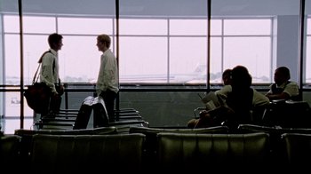 Movie still from “Primer” (2004), directed by Shane Carruth – A man walking through an airport with luggage; Wide shot, Over the shoulder angle