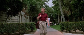 Movie still from “Prince of Darkness” (1987), directed by John Carpenter – A man walking down a sidewalk holding a brown bag; Wide shot, Low angle