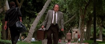Movie still from “Prince of Darkness” (1987), directed by John Carpenter – A man in a suit and tie holding a briefcase walking down a sidewalk; Medium shot, Low angle