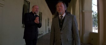 Movie still from “Prince of Darkness” (1987), directed by John Carpenter – Two men in suits and ties standing next to each other; Medium shot, Low angle