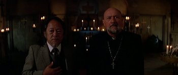 Movie still from “Prince of Darkness” (1987), directed by John Carpenter – Two men standing next to each other in front of candles; Medium shot, Low angle