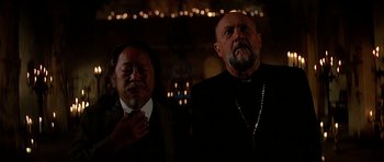 Movie still from “Prince of Darkness” (1987), directed by John Carpenter – Two men standing next to each other in front of candles; Medium shot, Low angle