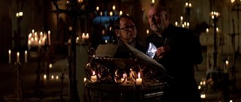 Movie still from “Prince of Darkness” (1987), directed by John Carpenter – Two men standing in front of a table with lit candles on it; Close Up shot, Low angle